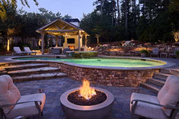 Backyard firepit with seating, illuminated pool, and custom stonework.