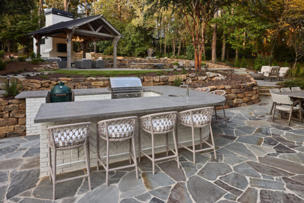 Modern outdoor kitchen with built-in grill, stone countertops, and bar seating.